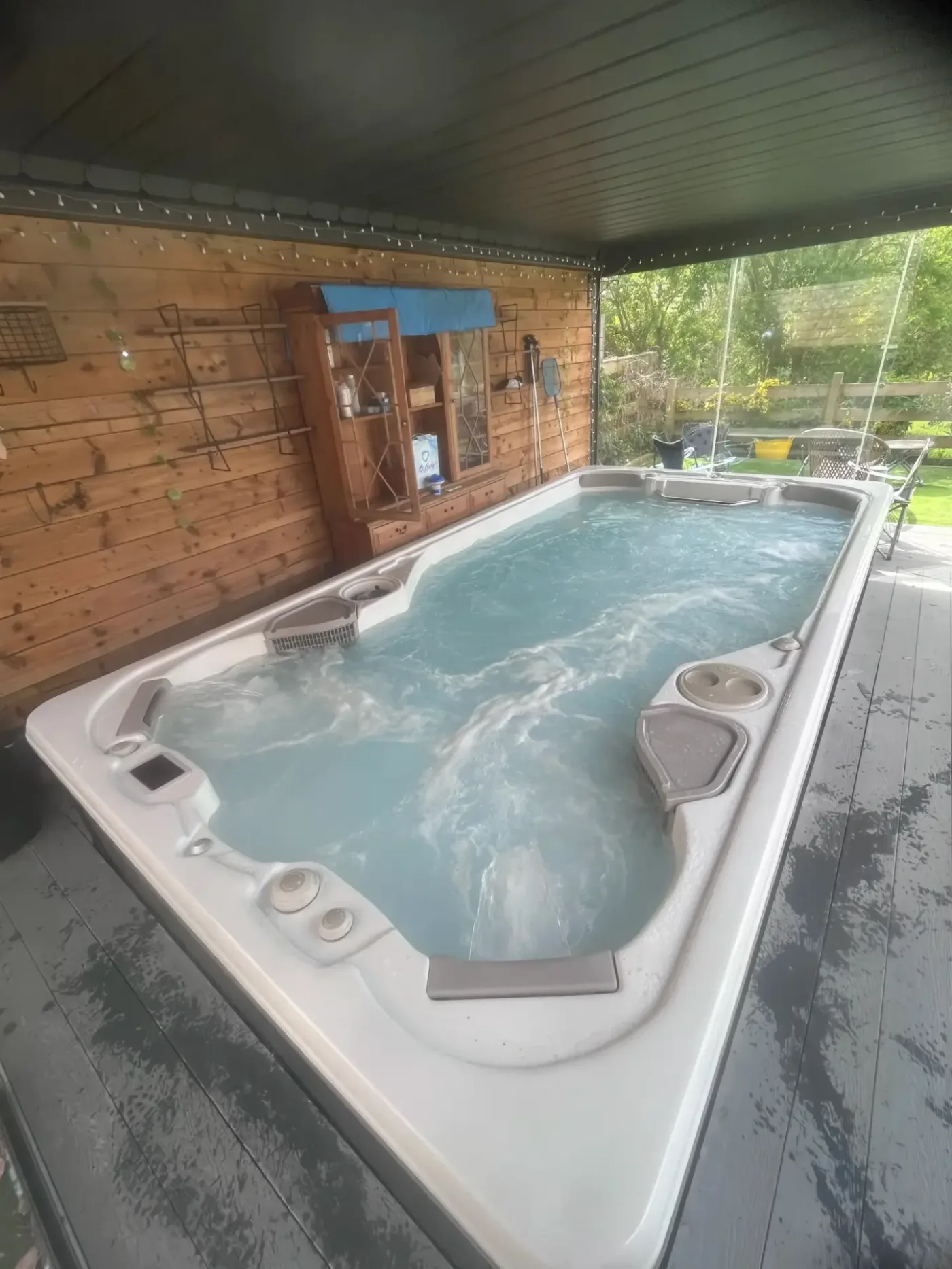 Long swim spa with bubbling water beside a timber garden building